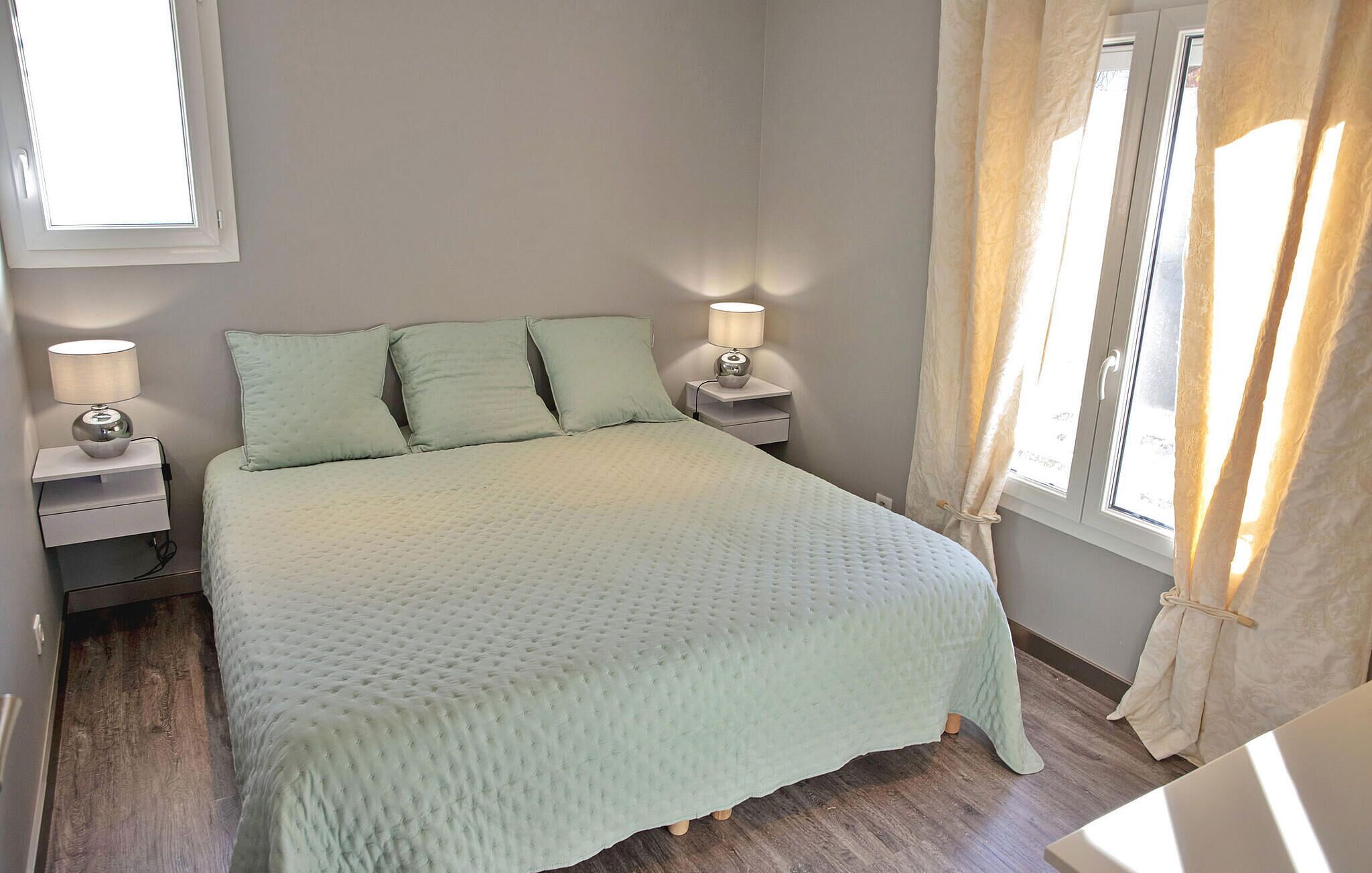 Una cama bien hecha con un cubrecolcha acolchado, dos lámparas de noche y una ventana con cortinas.