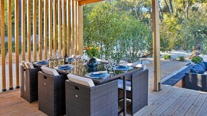 An outdoor dining area with wicker furniture, a wooden pergola, and a view of a garden with trees and shrubs.