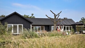 A modern house with a dark exterior, large windows, and a tree in the front yard. - Awesome home in Bogense with WiFi (Bogense)