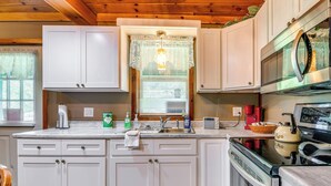 Una cocina con armarios blancos, un lavamanos de acero inoxidable, un microondas y una estufa.