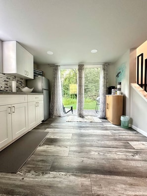A modern kitchen with white cabinets, a built-in oven, and a view of a garden through large windows.