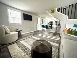 A modern living room with a sofa, a coffee table, and a dining area in the background.