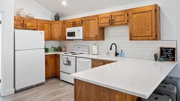 A modern kitchen with wooden cabinets, a white refrigerator, a microwave, a stove, and a large island with a sink. - Cozy 2-bedroom 2nd story condo with AC, fitness room and WiFi in St. George Utah (St. George)