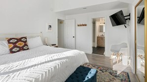 A bedroom with a large bed, a blue bench, a TV mounted on the wall, and a door leading to a bathroom. - Cozy 2-bedroom 2nd story condo with AC, fitness room and WiFi in St. George Utah (St. George)