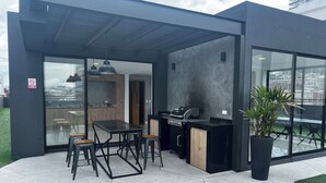 An outdoor kitchen area with a grill, dining table, and chairs. - Luxurious and comfortable suite close to La Carolina Park (Quito)