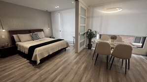 A modern bedroom with a large bed, bedside tables, a desk with chairs, a potted plant, and a view of the outside. - Luxurious and comfortable suite close to La Carolina Park (Quito)