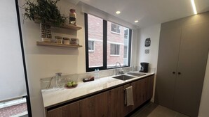 A modern kitchen with a marble countertop, wooden cabinets, a sink, and a window with a view of a brick building. - Luxurious and comfortable suite close to La Carolina Park (Quito)