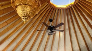 Una cama con cabecera, ventilador de techo y alfombra de piel en una habitación con vigas de madera y ventana.