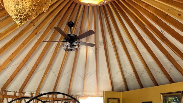 Interior de una yurta con cama, ventilador de techo y kitchenette.