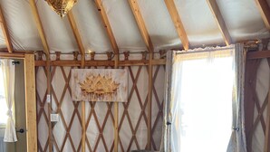 Una sala de estar acogedora con techo de madera, un sofá de cuero negro con cojines coloridos, una mesa de centro redonda de madera y una obra de arte colgada en la pared.