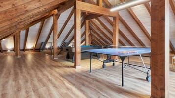 An attic room with wooden beams, a ping pong table, and a ceiling fan.