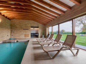 Una piscina con sillas de descanso, vigas de techo de madera y ventanas amplias.