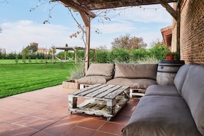 Un patio exterior con mesa de madera, sofá y una pérgola.