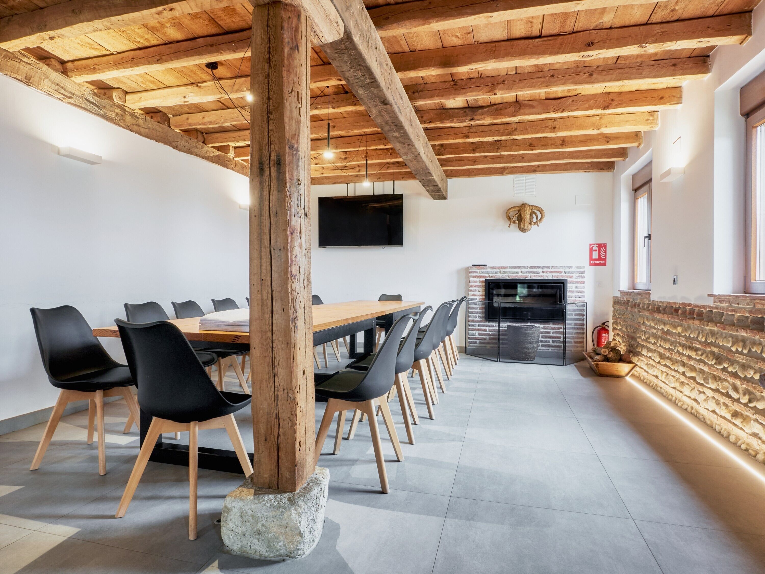A conference room with a long table, black chairs, a stone pillar, a fireplace, and a television on the wall.