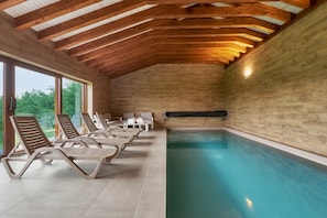 Un interior de madera con piscina, tumbonas y grandes ventanales.
