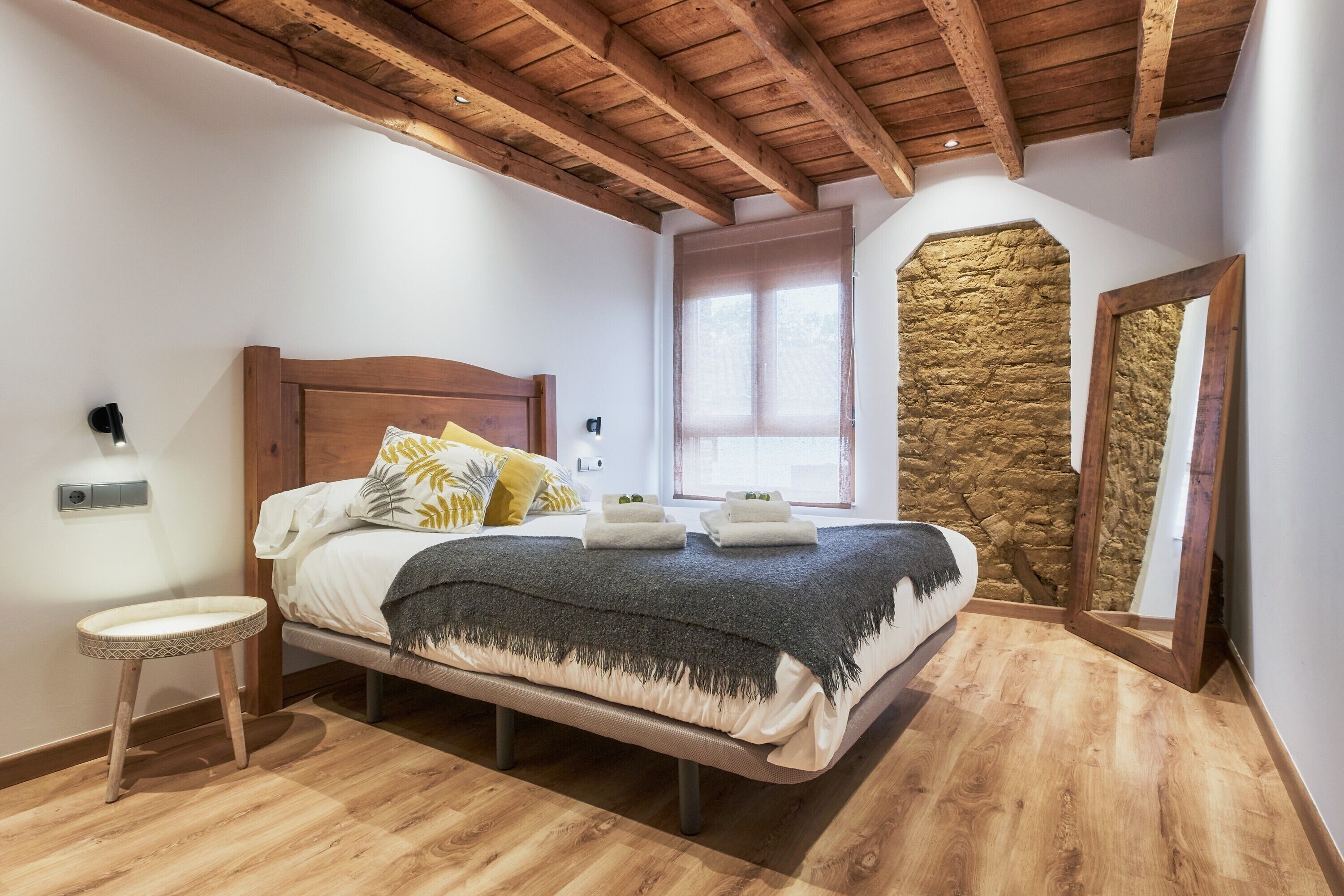 Et soveværelse med træloft, stenvæg, seng med puder og et natbord.