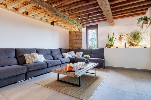 Una sala de estar con un sofá gris oscuro, una mesa de centro de madera con velas y una pared de piedra.