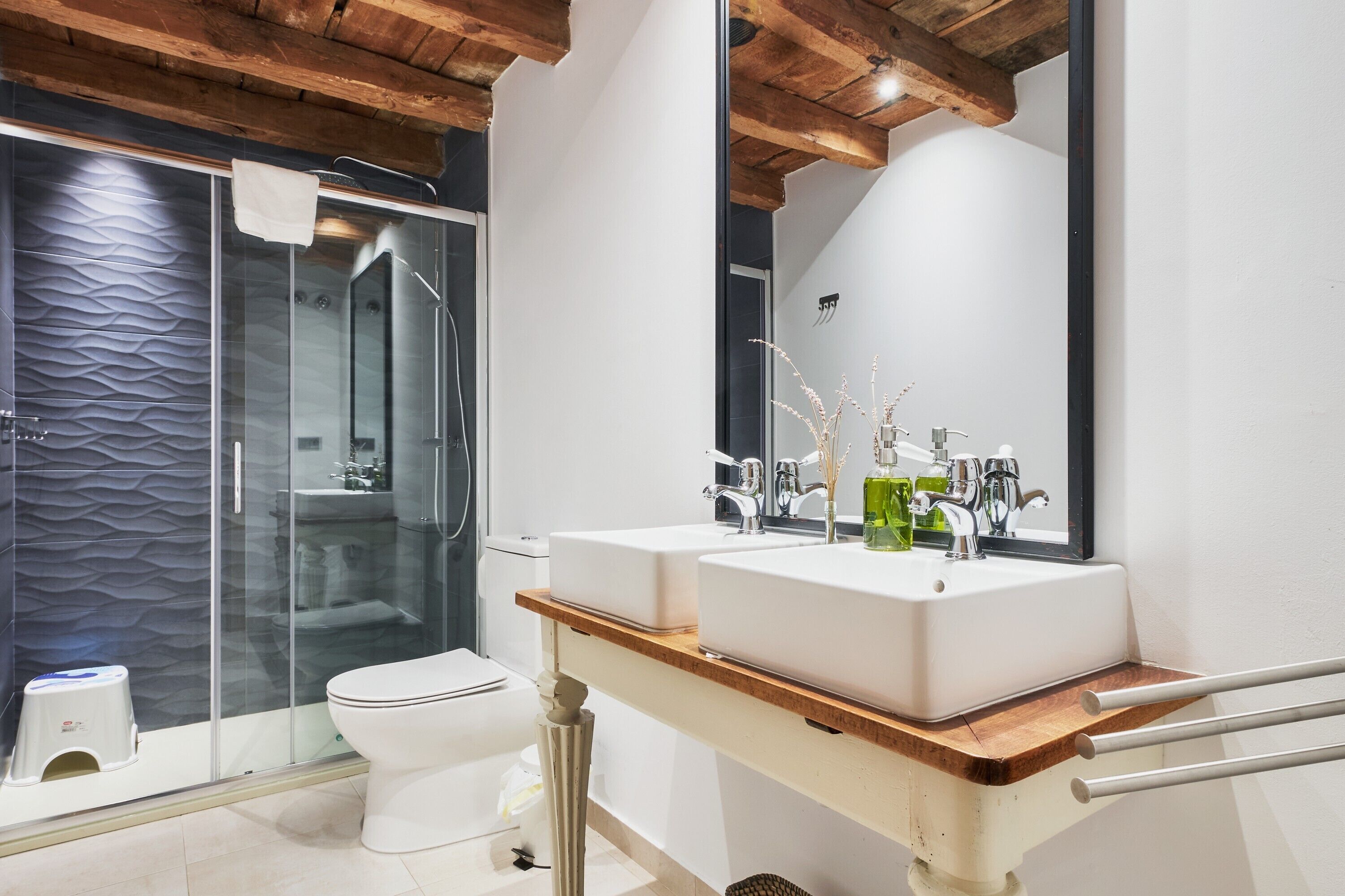 Ein modernes Badezimmer mit Duschkabine aus Glas, einer weißen Toilette und einem Holzwaschtisch mit zwei Becken.