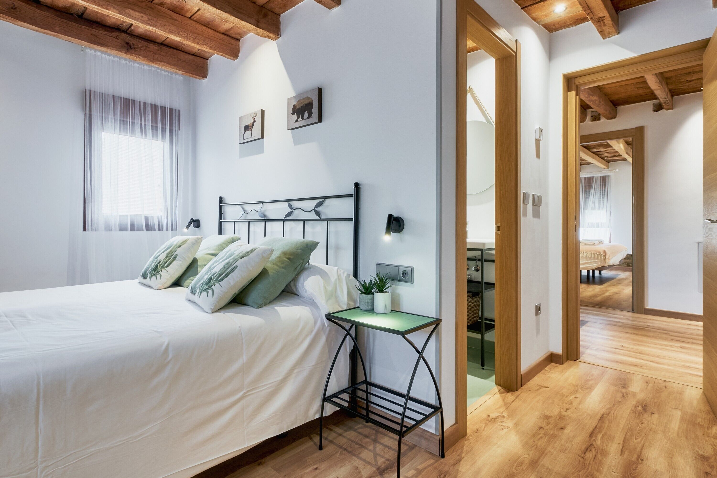 Un dormitorio con cama, mesita de noche y ventana con cortinas traslúcidas.