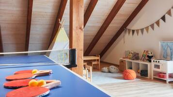 Ein Zimmer mit Tischtennisplatte, Holzmöbeln, einer kleinen Spielecke und einer erhöhten Decke.