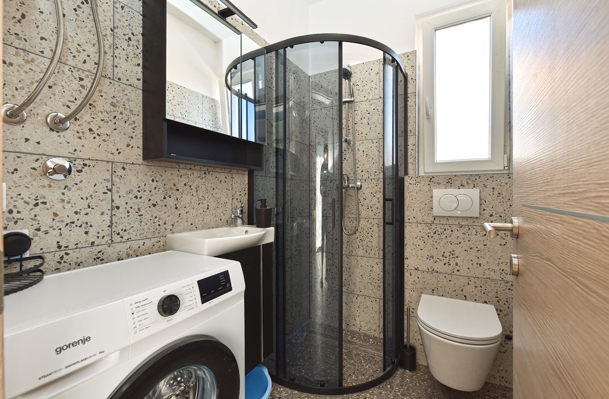 Een compacte badkamer met een douche in een glazen cabine, een witte wastafel en een toilet.