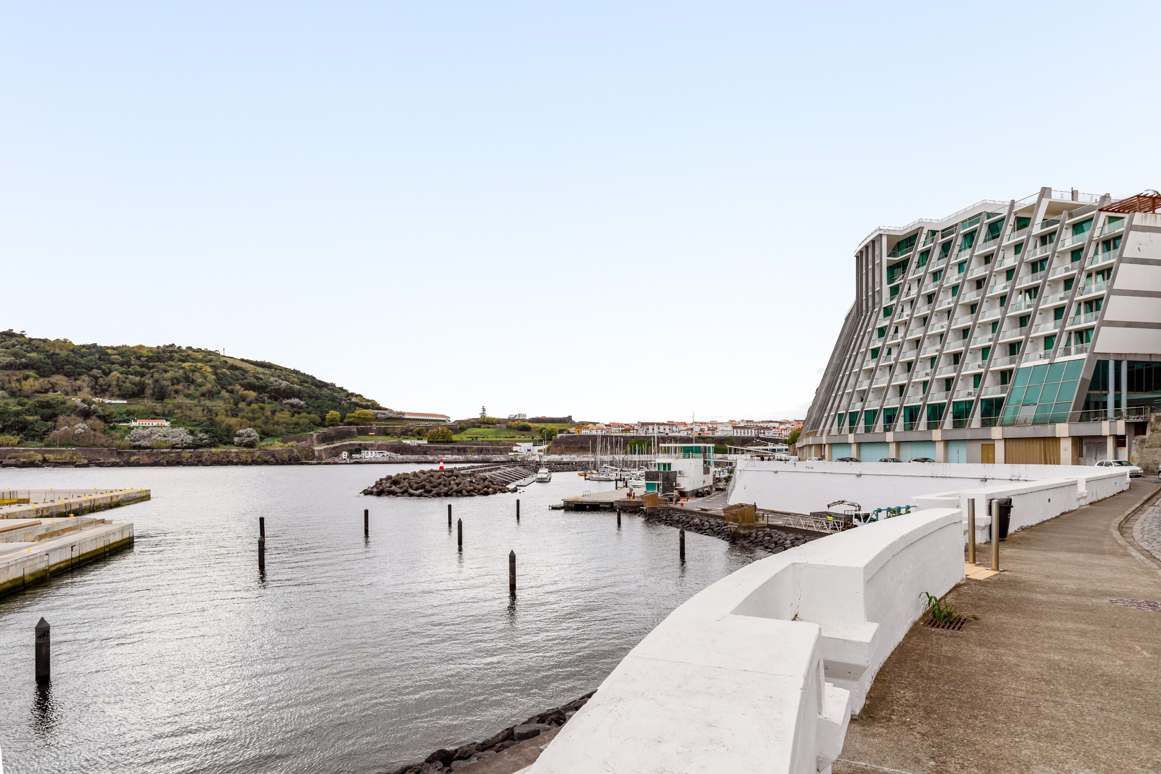 Un hotel moderno frente al agua, con un puerto deportivo y un paisaje montañoso al fondo.