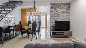 Un salon moderne avec un escalier, un coin repas et un téléviseur posé sur un meuble en bois.
