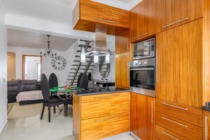 Une cuisine moderne avec des meubles en bois, un four encastré et un coin repas comprenant une table et des chaises.