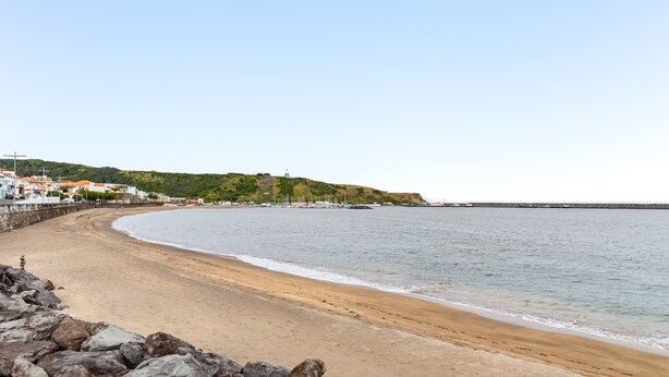 Une plage avec un rivage rocheux, une plage de sable en forme de croissant et des bâtiments en arrière-plan.