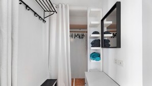 A bathroom with a shower, a bench, a mirror, and a shelf with folded towels.