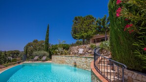 Una piscina cristalina con paredes de piedra, una escalera de piedra y vistas a árboles y un edificio al fondo.