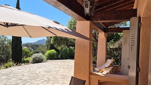 Un patio al aire libre con mesa y sillas, una zona de estar cubierta y vistas del paisaje circundante.
