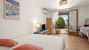 Habitación de hotel con cama, escritorio con lámpara, televisión, ventana con cortinas y puerta que da a un área exterior.