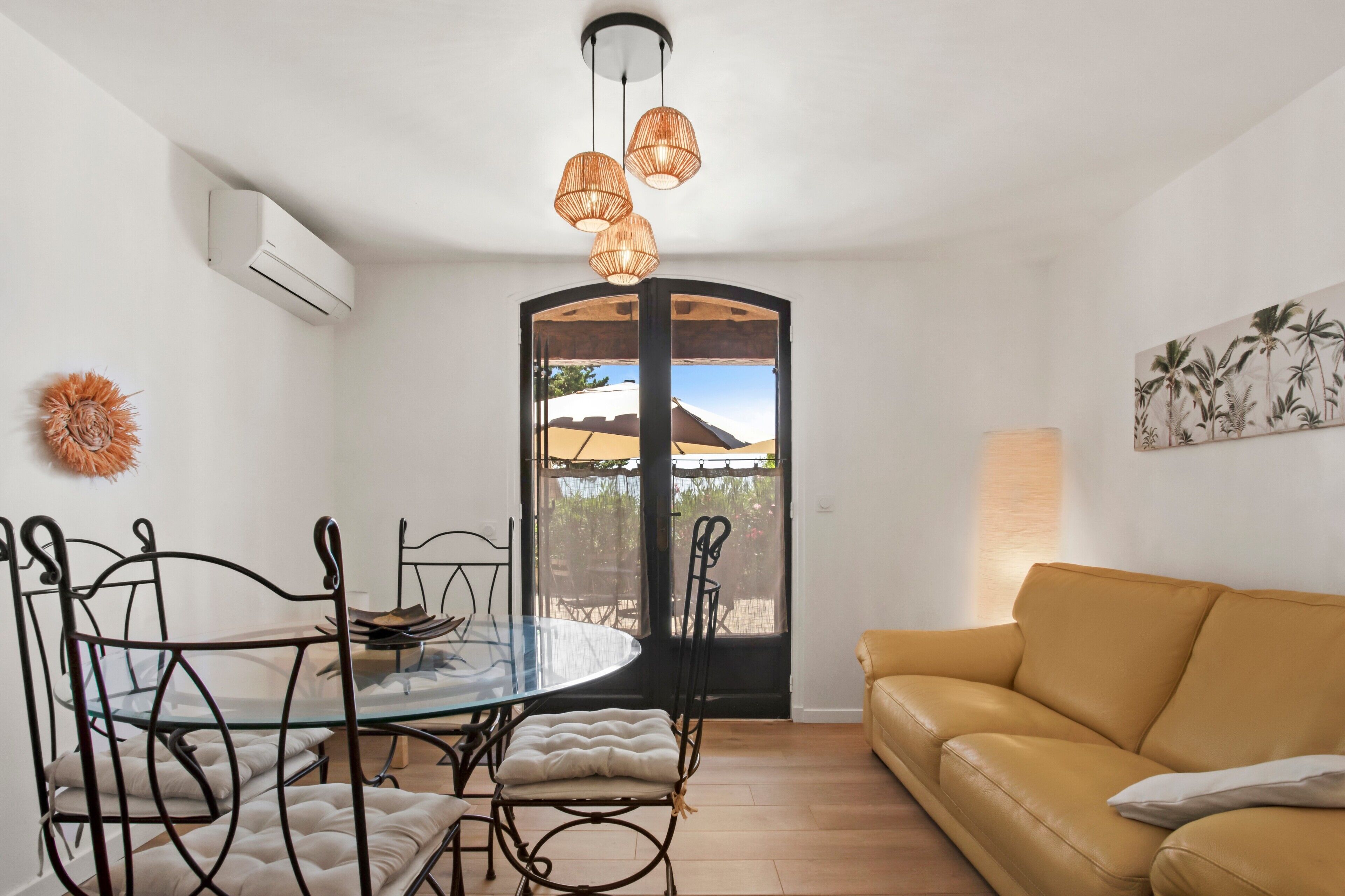 A dining area with a glass table and chairs, a sofa, and a view through a glass door.