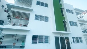 A multi-story building with white exterior walls, multiple balconies with metal railings, and a green vertical stripe on one side. - Senderos del botánico  (Santiago de los Caballeros)