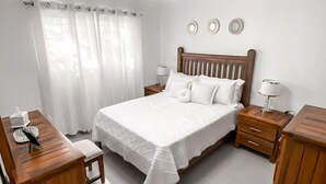 A neatly arranged bedroom with a large bed, bedside tables, a desk, and a ceiling fan. - Senderos del botánico  (Santiago de los Caballeros)