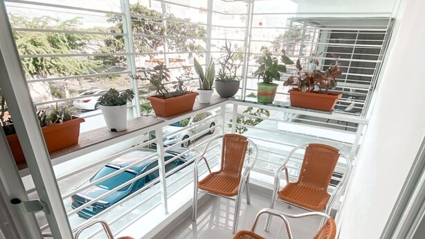 A balcony with wicker chairs, potted plants, and a view of parked cars and greenery. - Senderos del botánico  (Santiago de los Caballeros)