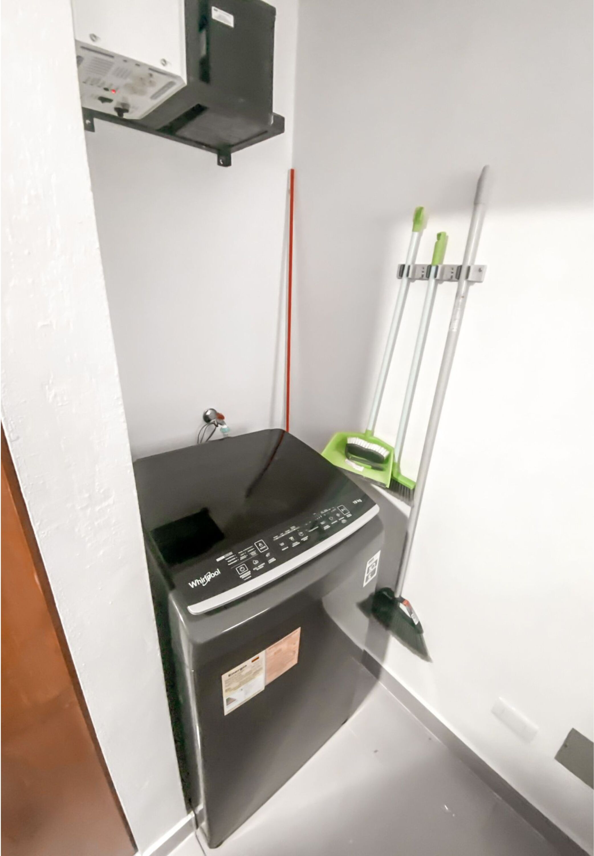 A compact kitchen with a Whirlpool dishwasher, a small countertop, and a green mop leaning against the wall.