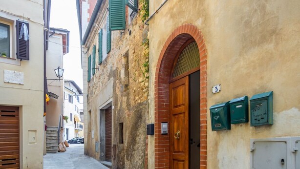 A narrow street with a building featuring a wooden door, a brick archway, and a mailbox.