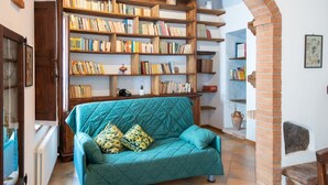 A cozy living room with a teal sofa, a bookshelf filled with books, and a rustic brick wall.