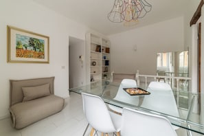 Un espace repas moderne avec une table en verre, des chaises blanches, un canapé et un luminaire décoratif.