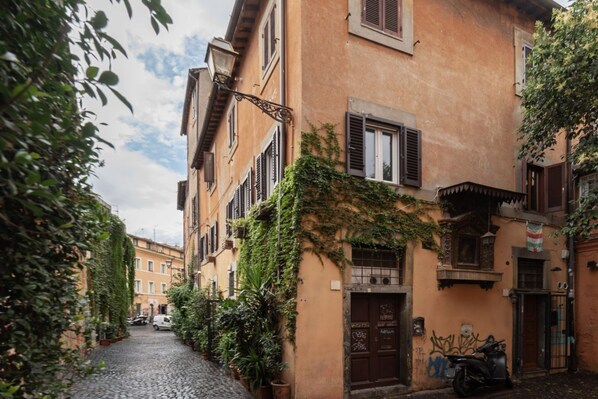 A narrow cobblestone street flanked by buildings with shutters and ivy.