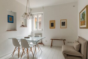 A modern dining area with a glass table, white chairs, and a hanging light fixture.