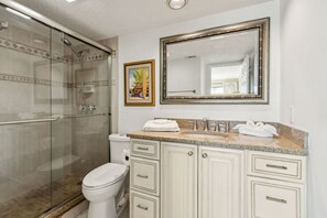 Een badkamer met een douchecabine van glas, toilet, wastafel met spiegel en kastjes.