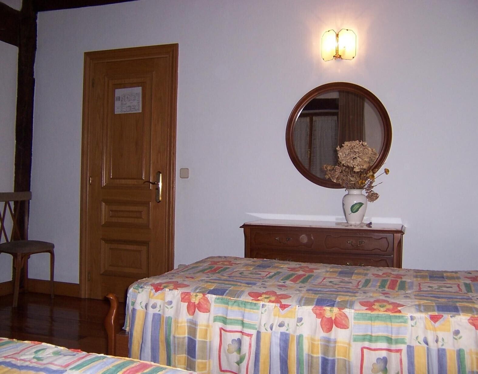 A bedroom with a wooden door, a dresser with a mirror, and a floral bedspread.