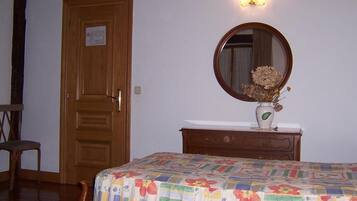 A bedroom with a wooden door, a dresser with a mirror, and a floral bedspread.