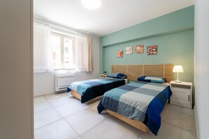 A bedroom with two beds, a window with curtains, a radiator, and artwork on the wall.