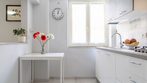 Une cuisine moderne avec des meubles blancs, un plan de travail blanc, un évier, une horloge et une fenêtre.