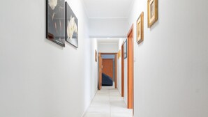 Un couloir aux murs ornés de tableaux encadrés, doté d’un sol carrelé et terminé par une porte.