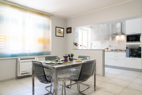 A modern kitchen with white cabinets, a built-in oven, and a dining area with a table and chairs.